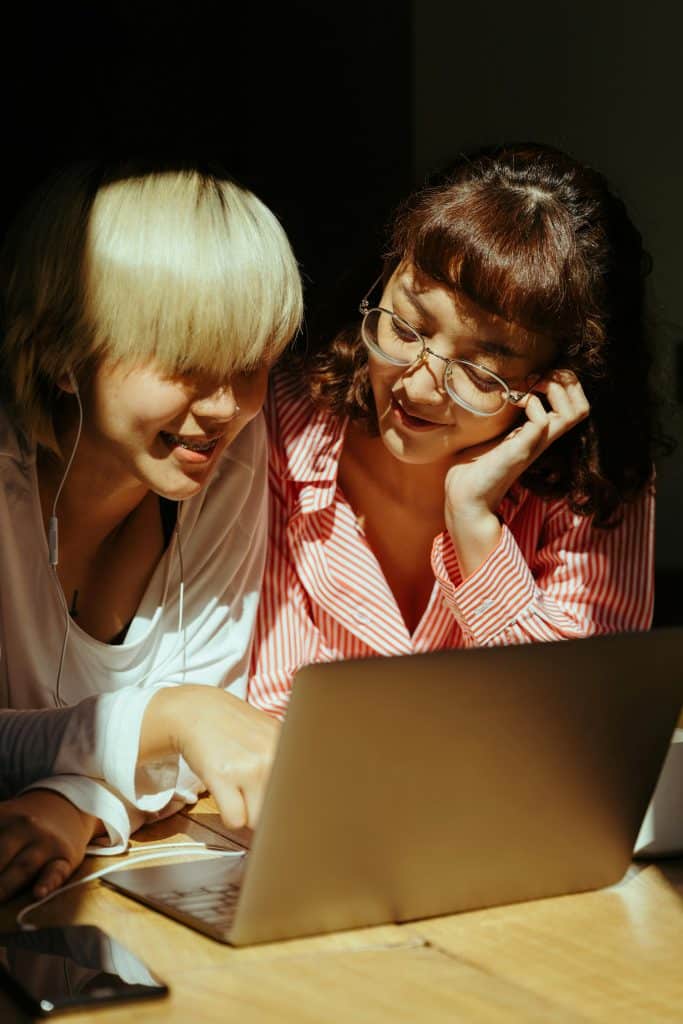 Friends enjoying a cozy moment together, sharing a laptop and laughter in warm light.