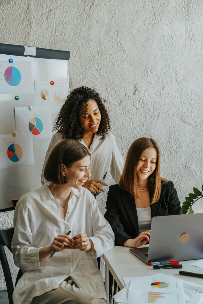 Three women collaborating in a modern office, focused on analytics and teamwork.