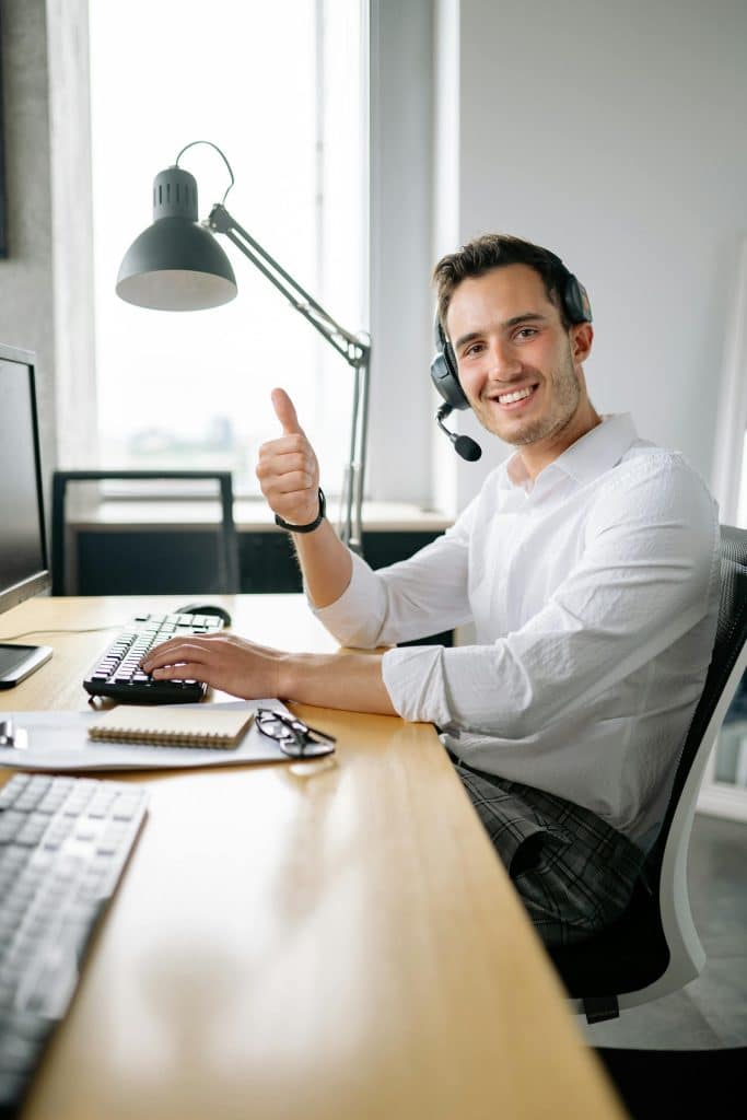 Cheerful young man at a bright, organized desk, smiling and engaged in productive work.
