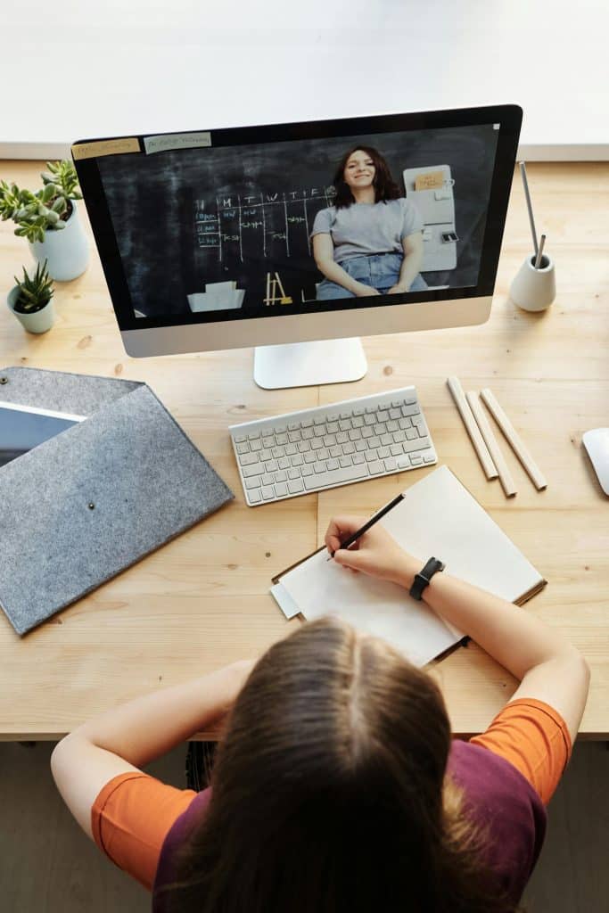 Young woman engaged in virtual learning at a wooden desk with plants and organized materials.