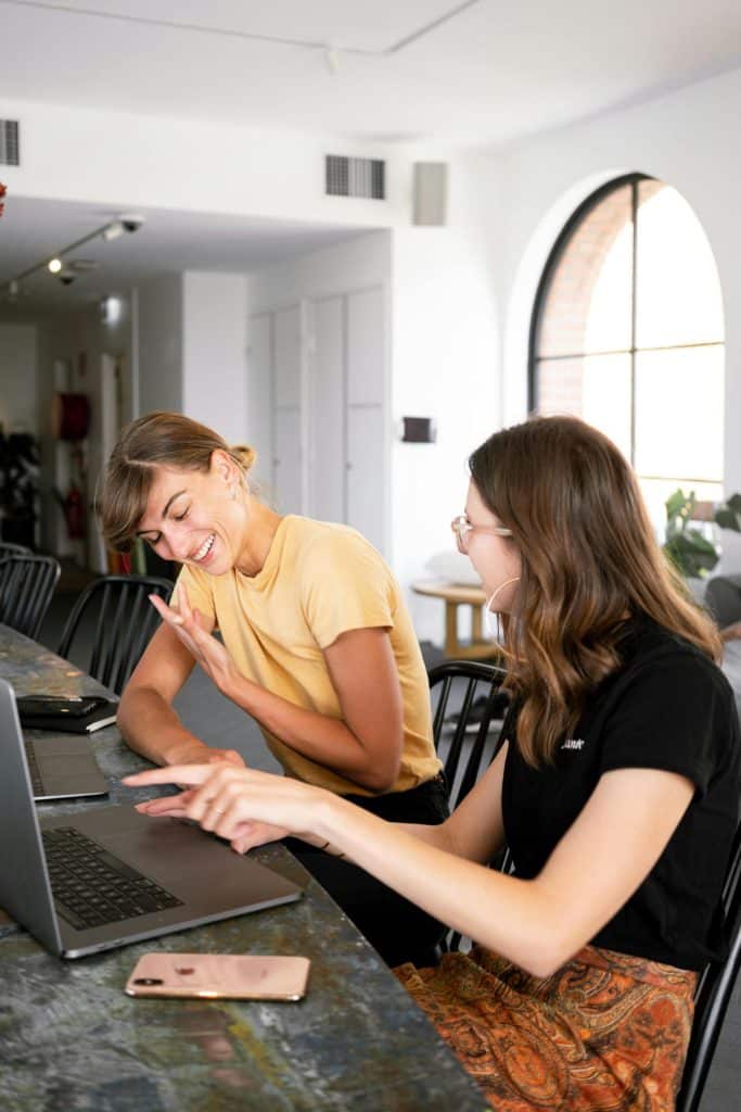 Women collaborating and discussing ideas in a bright, modern workspace with a laptop.
