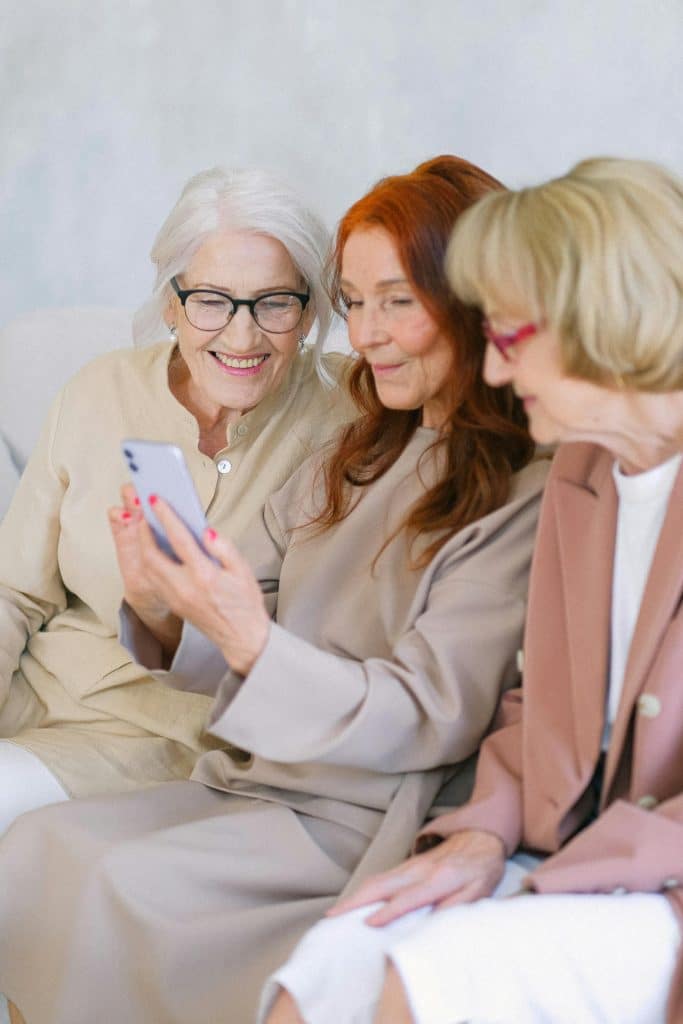Three women joyfully connect over a smartphone, showcasing friendship on a cozy sofa.