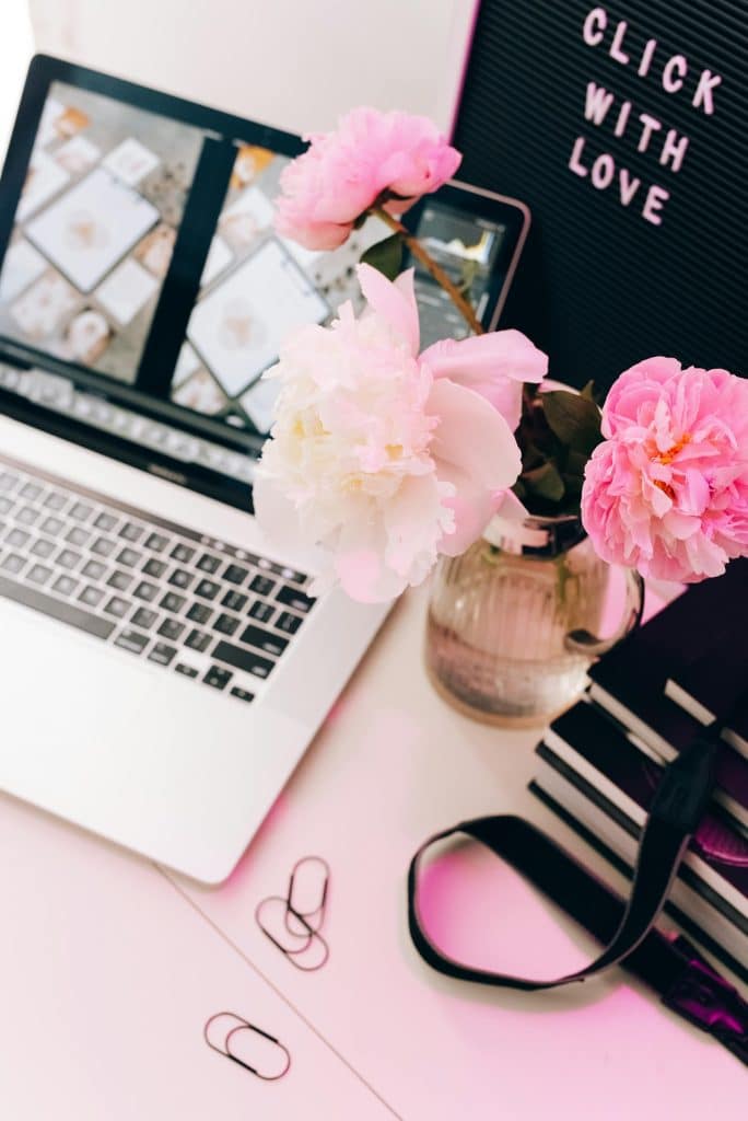 Stylish creative workspace with flowers and modern laptop displaying vibrant design projects.
