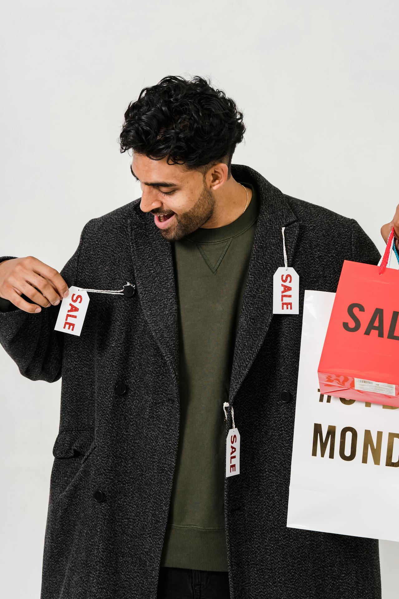 Young man joyfully shopping, wearing a stylish overcoat and holding a SALE MONDAY bag.