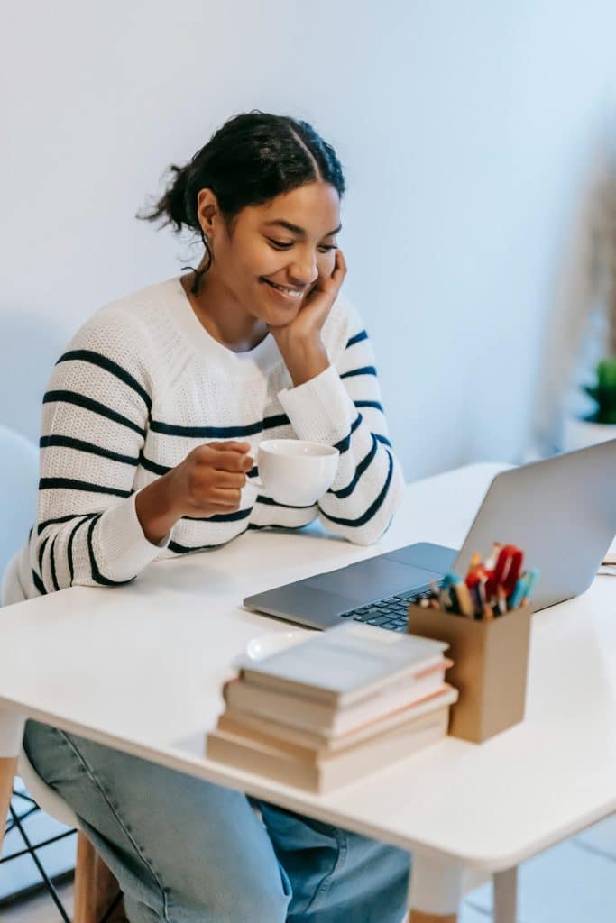 Young woman smiling at laptop in cozy, organized workspace with books and greenery.