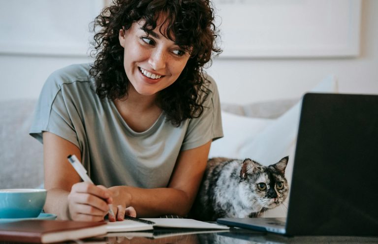 Young woman working on a laptop with her gray cat in a cozy home office setting.