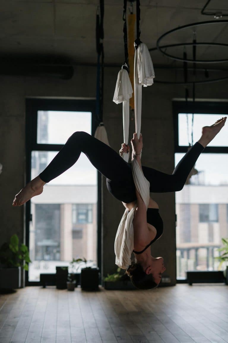 Aerial silks performer suspended upside down in a sunlit studio, showcasing strength and grace.