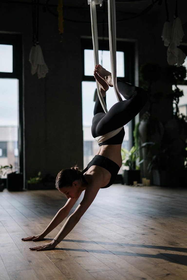 Aerial yoga practitioner gracefully suspended, showcasing strength and balance in a serene, sunlit studio.