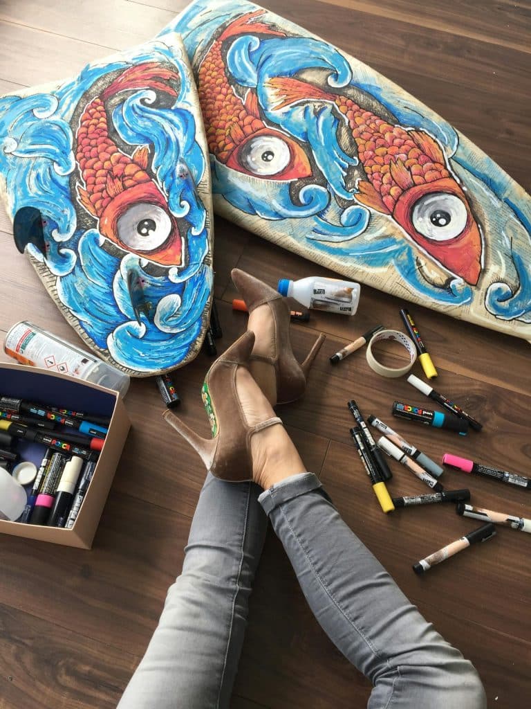 Colorful surfboard art with koi fish in a vibrant creative workspace.