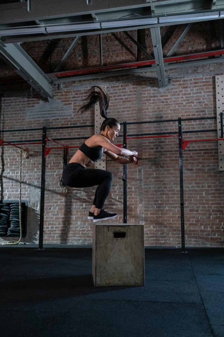 Athletic woman demonstrates strength and agility in a box jump at a modern gym.
