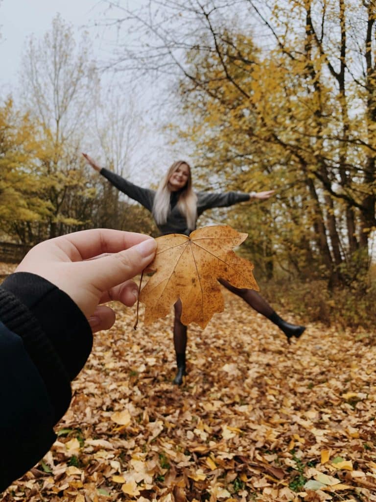 Joyful woman in autumn leaves, embracing natures beauty with vibrant golden hues.
