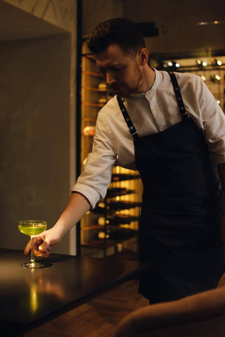 Stylish bartender presenting a vibrant green cocktail in an upscale wine cellar setting.