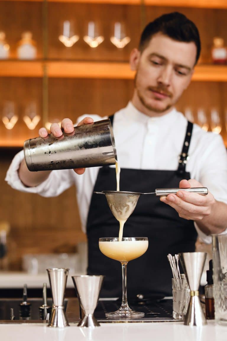 Skilled bartender pours a pale yellow cocktail, showcasing mixology artistry in a modern bar.