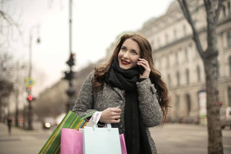 Joyful woman shopping in a vibrant city, holding colorful bags on a cool day.