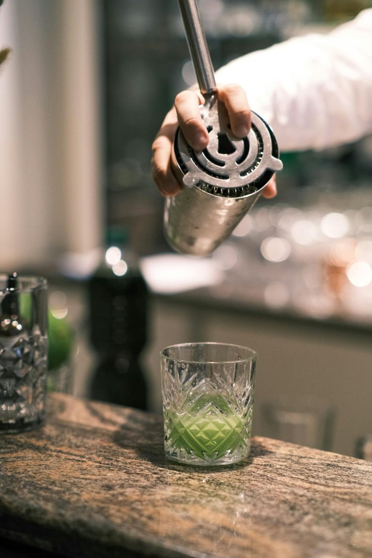 Elegant bartender pours vibrant green cocktail into etched glass, showcasing mixology artistry.