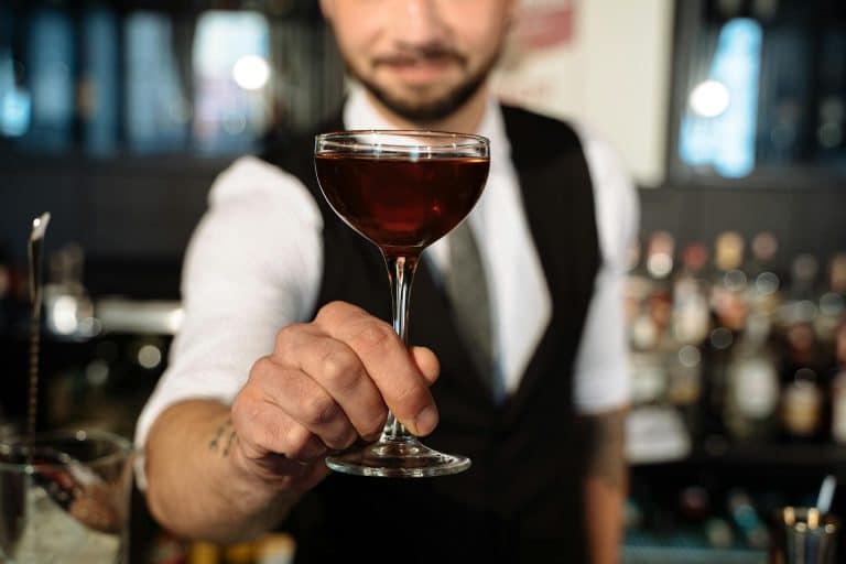 Expert bartender presents a rich cocktail in a classic coupe glass at an upscale bar.