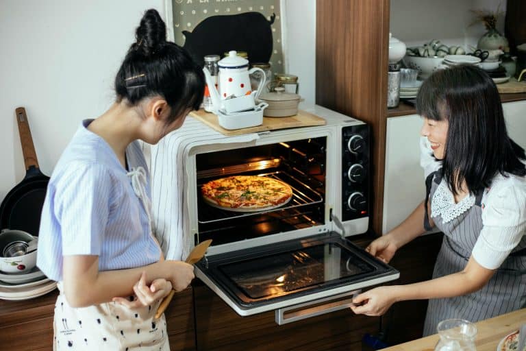 Two women joyfully cooking together, sharing laughter and a delicious, colorful pizza in a cozy kitchen.