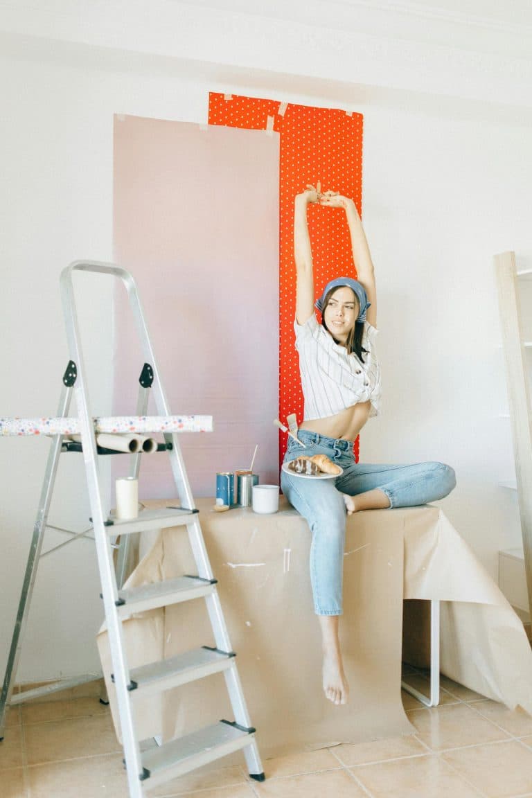 Young woman joyfully painting in a bright, creative space with vibrant colors and artistic tools.