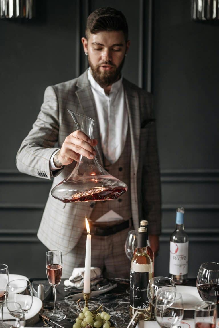 Sophisticated dining scene with a man decanting wine amidst elegant decor and candlelight.