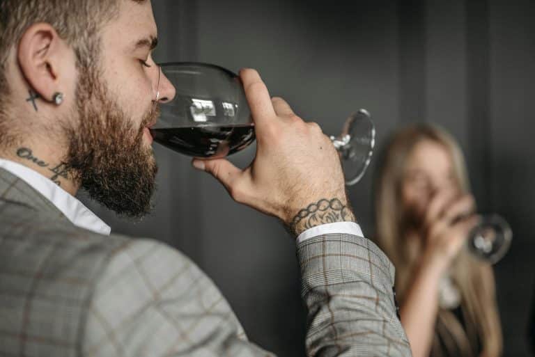 Sophisticated man in a gray suit savoring red wine at a stylish social gathering.