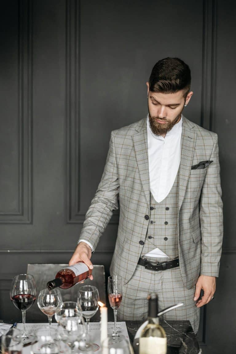 Stylishly dressed man pours wine at an elegant table, embodying sophistication and hospitality.