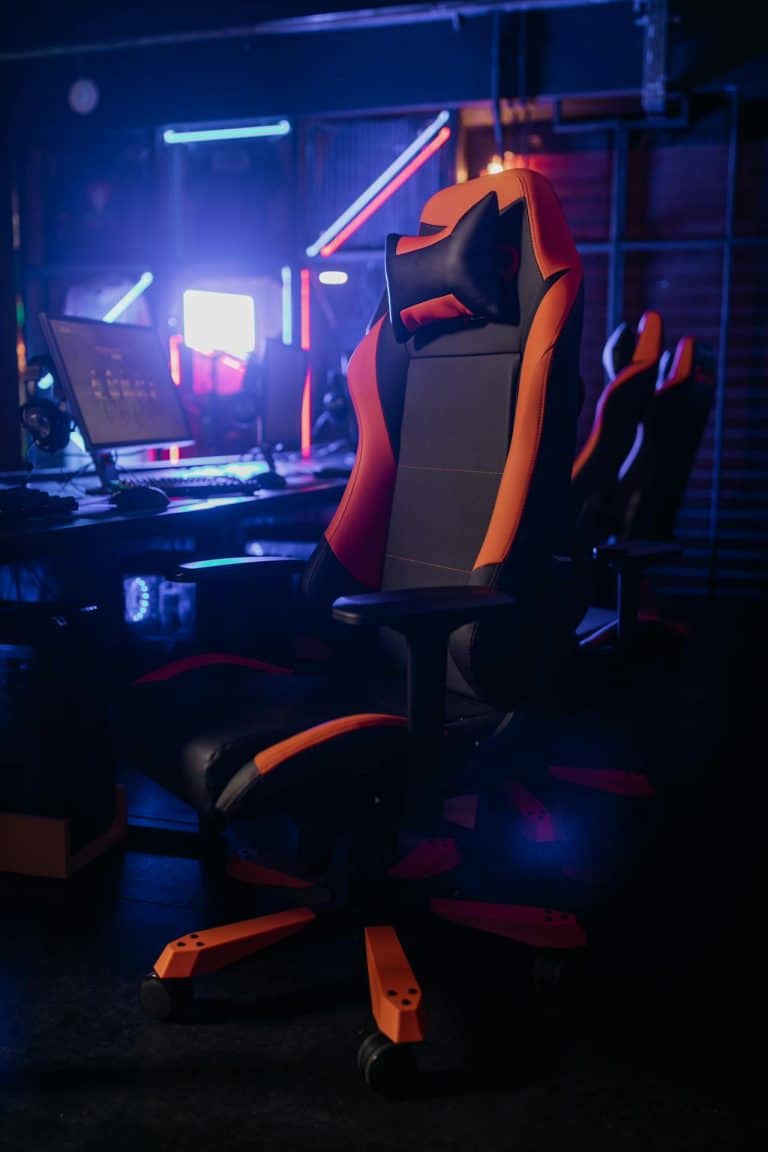 Black and orange ergonomic gaming chair in a vibrant neon-lit gaming room.