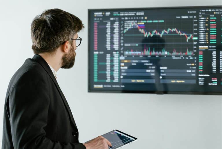 Professional analyst monitors financial trends on screen with tablet in modern workspace.