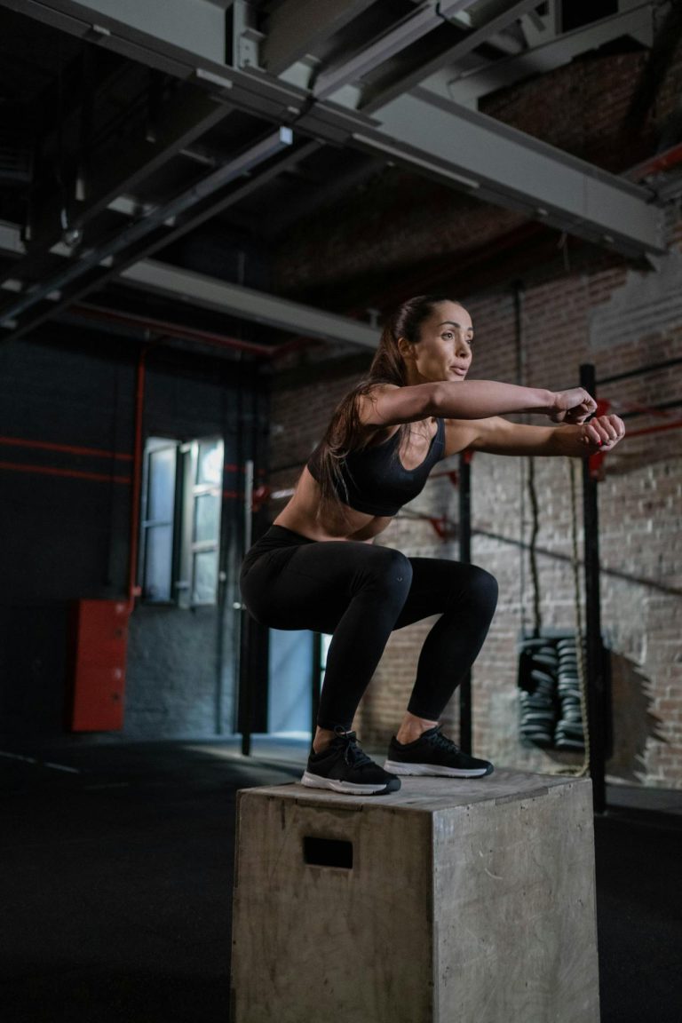 Woman performing a powerful squat on a concrete platform in a modern gym.