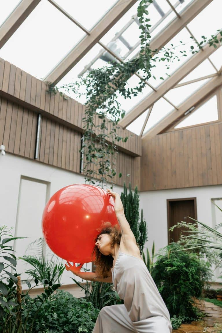 Joyful dancer with a red balloon in a modern indoor garden filled with greenery.