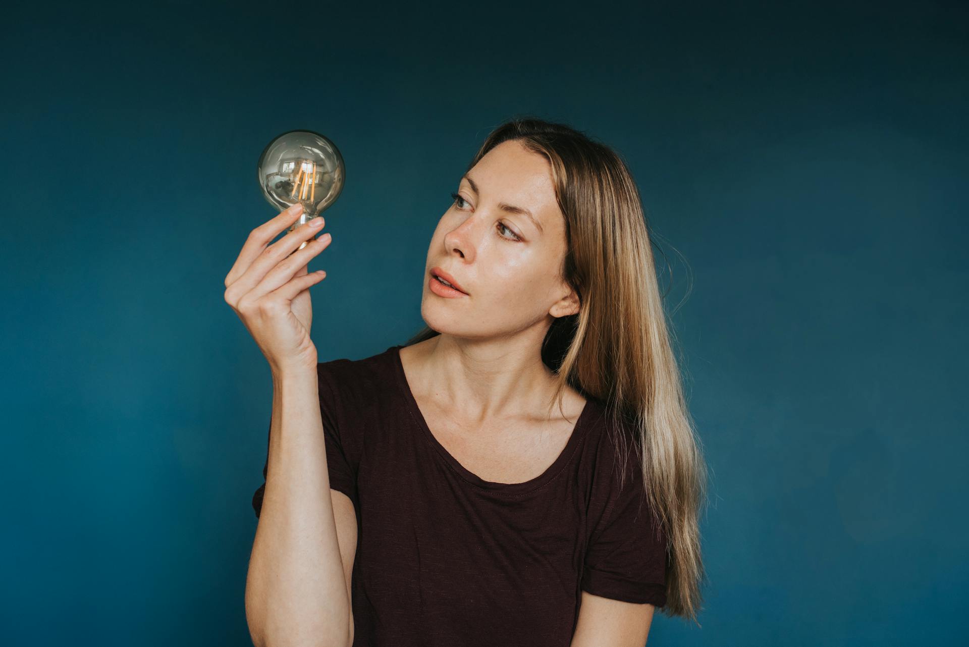 Woman contemplating creativity while examining a vintage light bulb against a dark blue background.