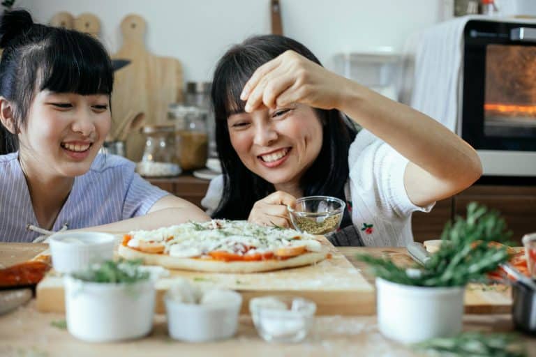 Two women joyfully make pizza together in a warm, inviting kitchen.