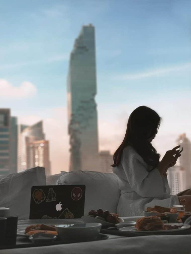 Luxury city retreat: Woman in robe enjoys breakfast and views amidst serene morning light.