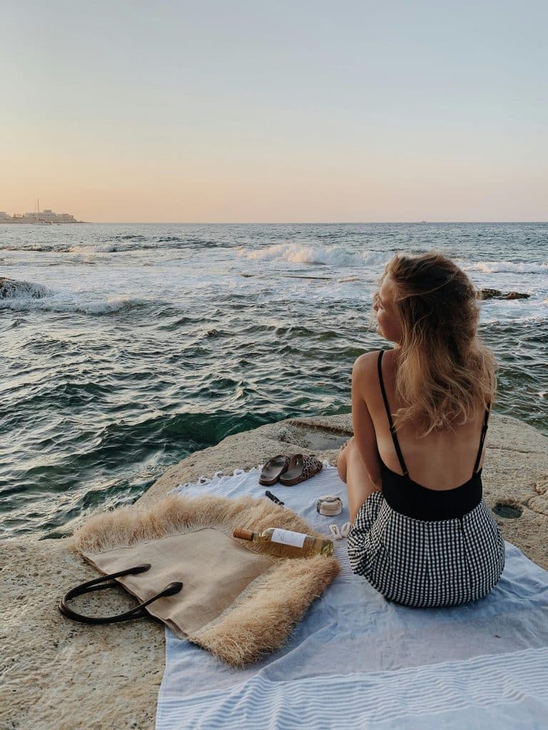 Young woman enjoys a tranquil seaside moment on a blanket during a stunning sunset.