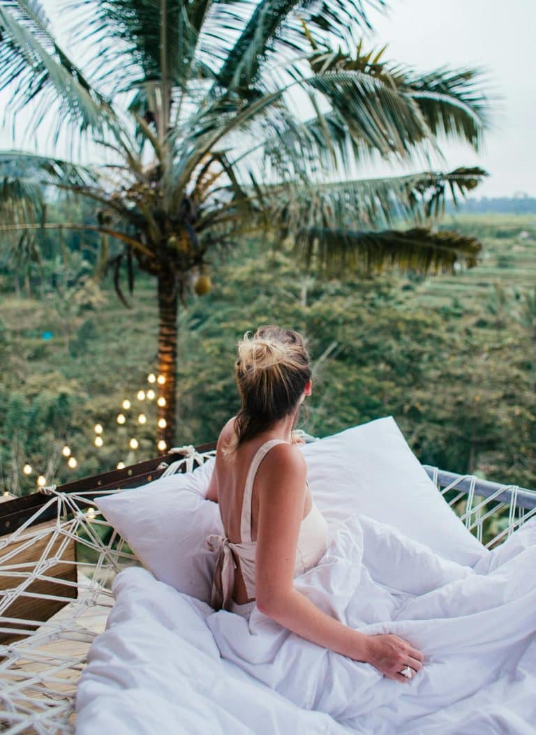Young woman relaxes on a balcony bed, enjoying peaceful views of lush rice paddies.