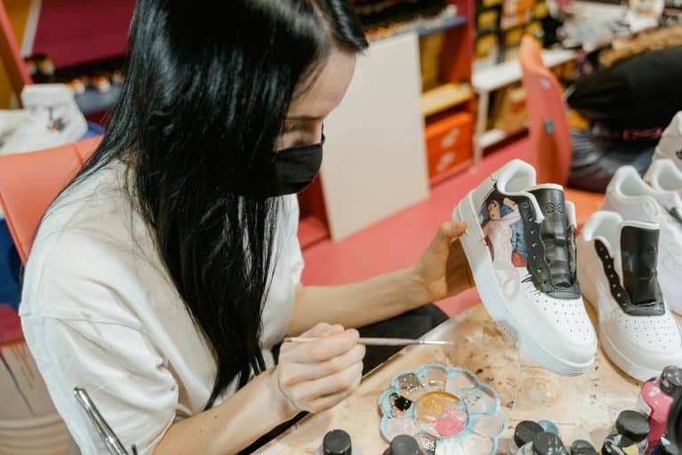 Young woman customizing sneakers with vibrant paints in her creative workspace.