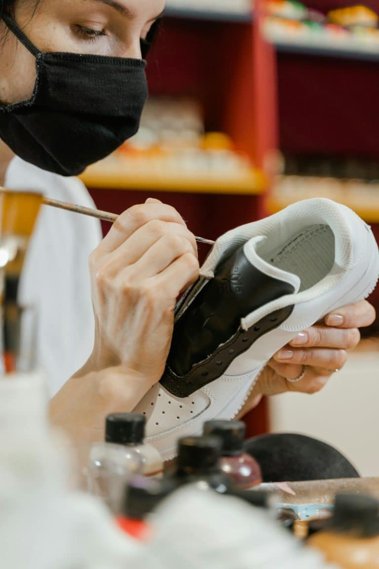 Artist customizes a white sneaker with black accents in a vibrant, organized workspace.