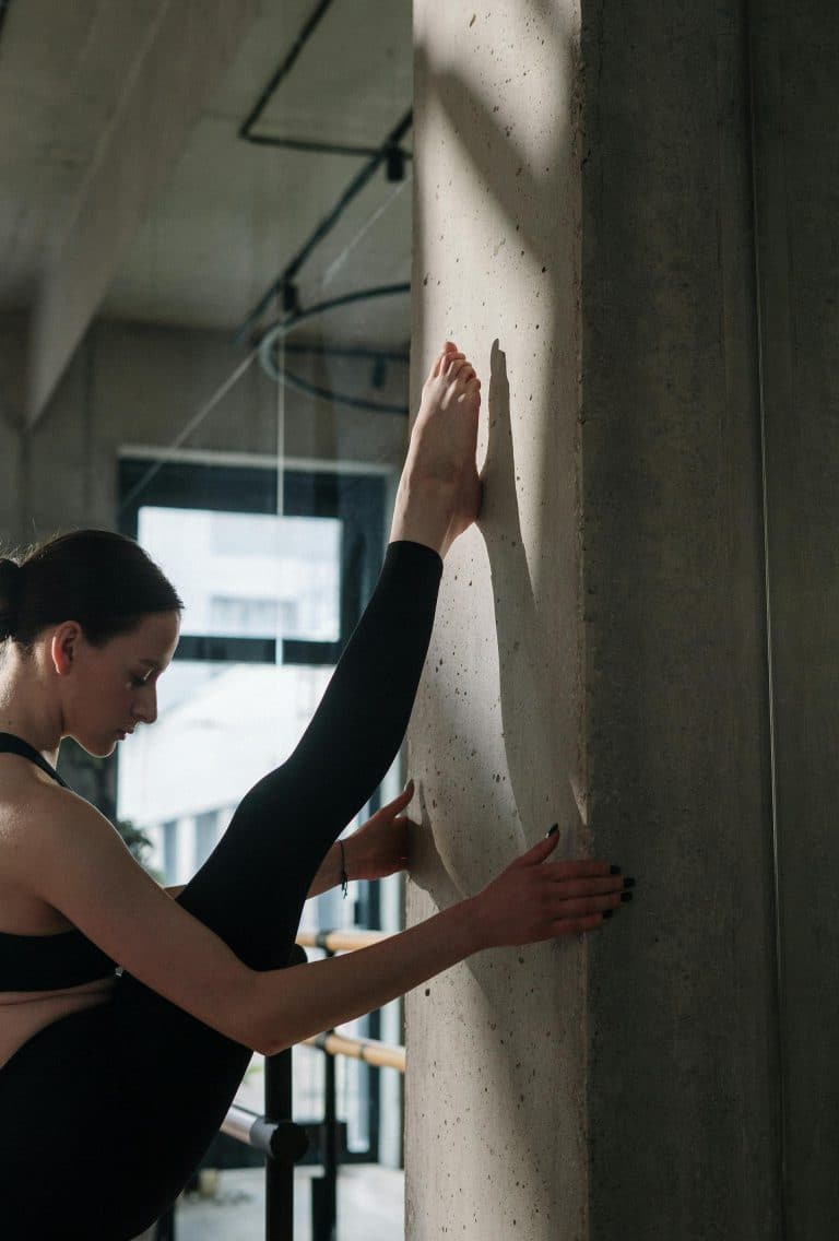 Young woman stretches against a concrete wall, showcasing flexibility and strength in a serene space.