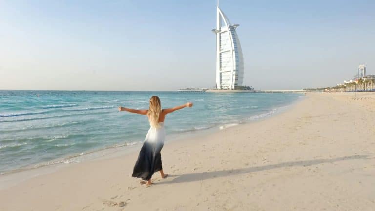 Woman joyfully embraces the beach at Dubais Burj Al Arab, enjoying the serene ocean view.