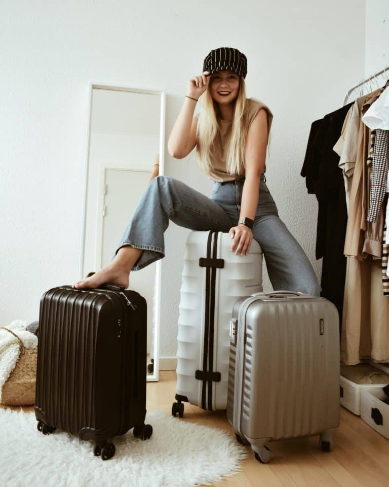 Joyful woman on suitcase, showcasing trendy travel style and carefree spirit in chic space.
