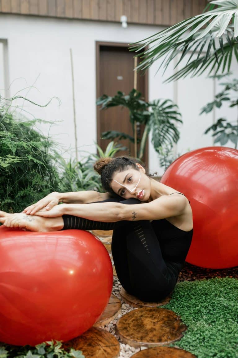 Woman stretching in a serene indoor space with red exercise balls and green plants.