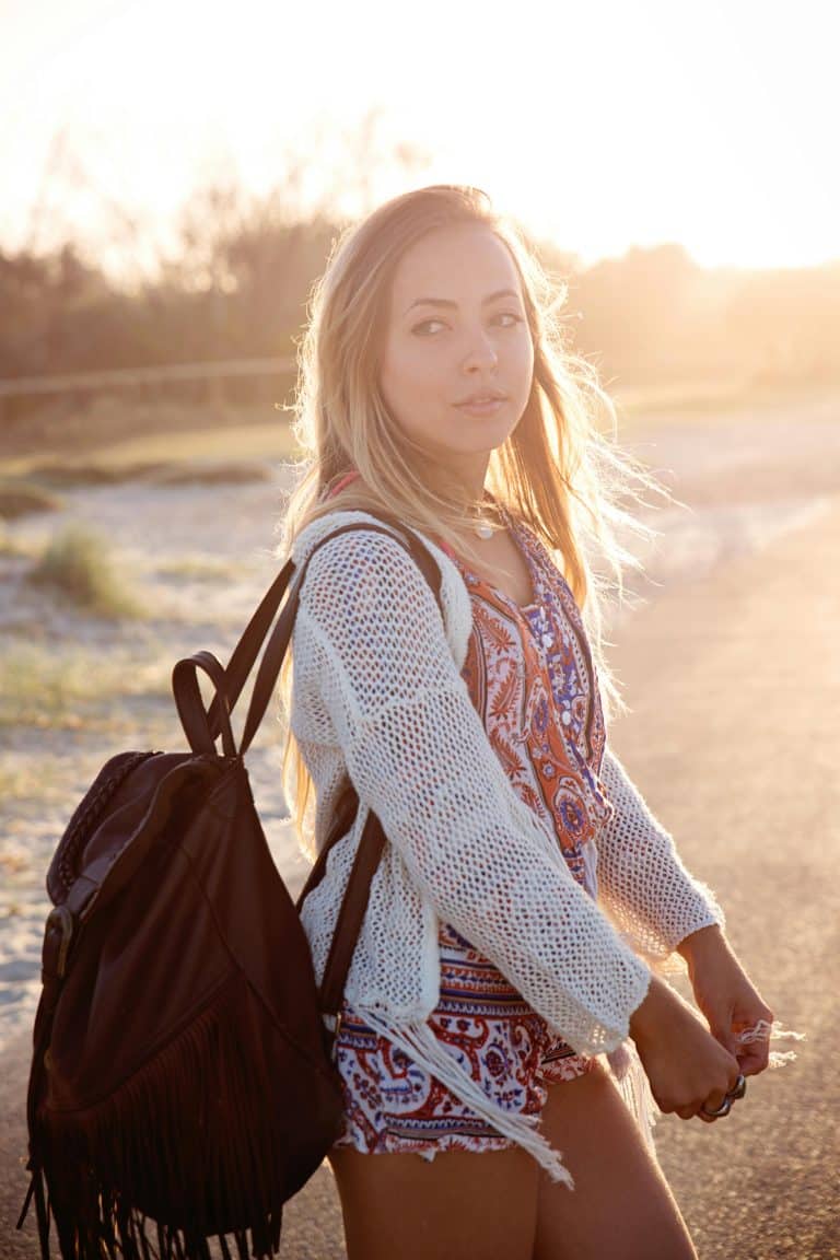Bohemian woman in sunlight, vibrant outfit and backpack, embracing natures serenity and youthful freedom.