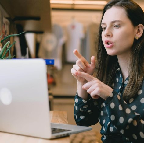 Young woman animatedly discussing in a bright, modern workspace during a virtual meeting.