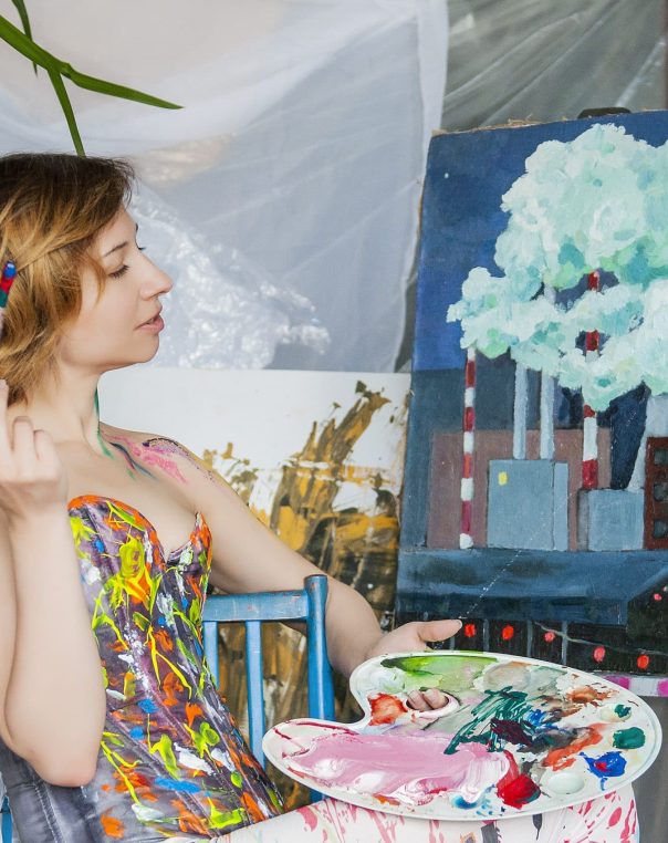 Young woman painting in a vibrant studio, exploring nature and industry through art.