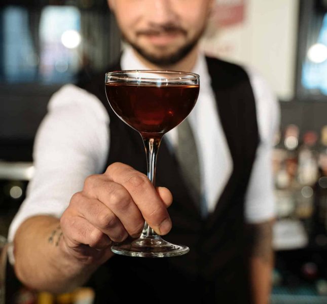 Expert bartender presents a rich cocktail in a classic coupe glass at an upscale bar.