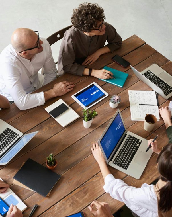 Diverse team collaborating around a wooden table, utilizing laptops and sharing ideas in a meeting.