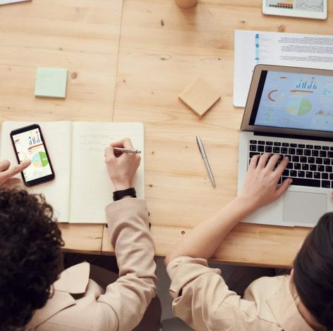 Two individuals collaborate at a wooden table, blending technology and creativity in a productive workspace.