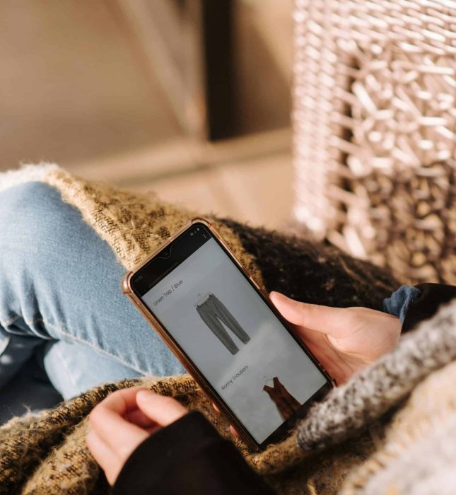 Cozy indoor shopping: a person draped in a blanket browsing fashion on their smartphone.