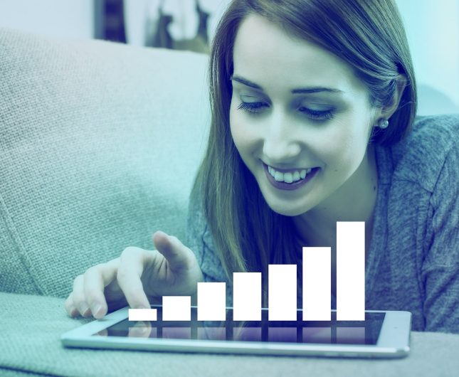 Young woman smiles on couch, using tablet with progress chart, highlighting technologys benefits.
