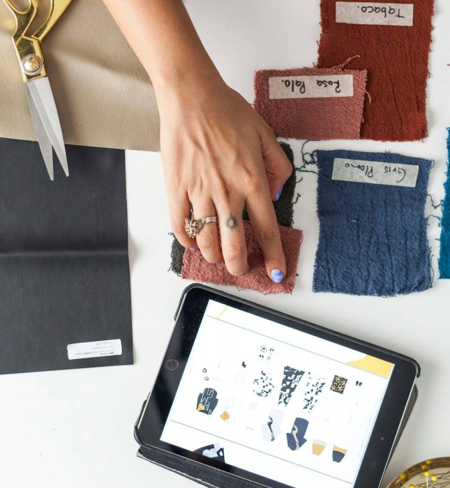 Vibrant creative workspace with digital designs, fabric swatches, tools, and embellishments for crafting.