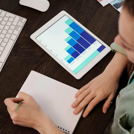Person in light green shirt analyzes data on tablet in a modern workspace.